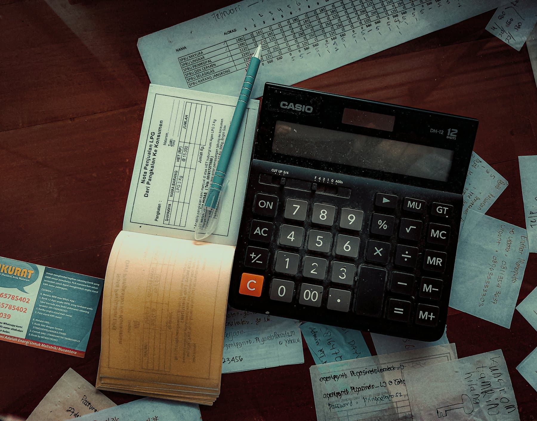 A calculator resting on a wooden desk beside paperwork