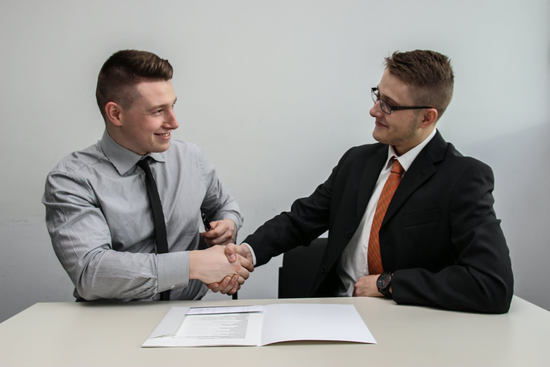 Two people shaking hands across a desk at the start of an engagement