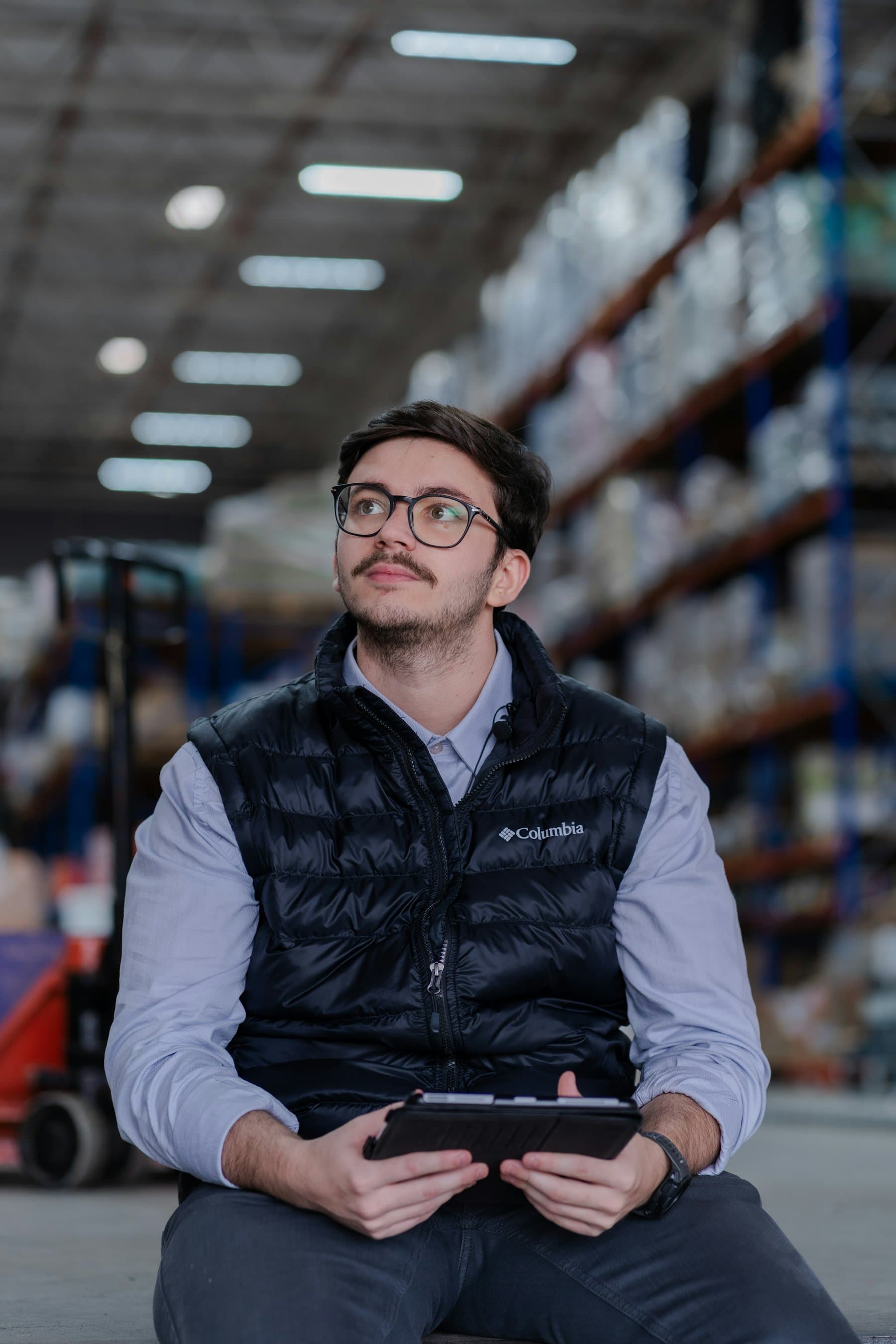 A warehouse worker holding a tablet and looking up at stock shelving