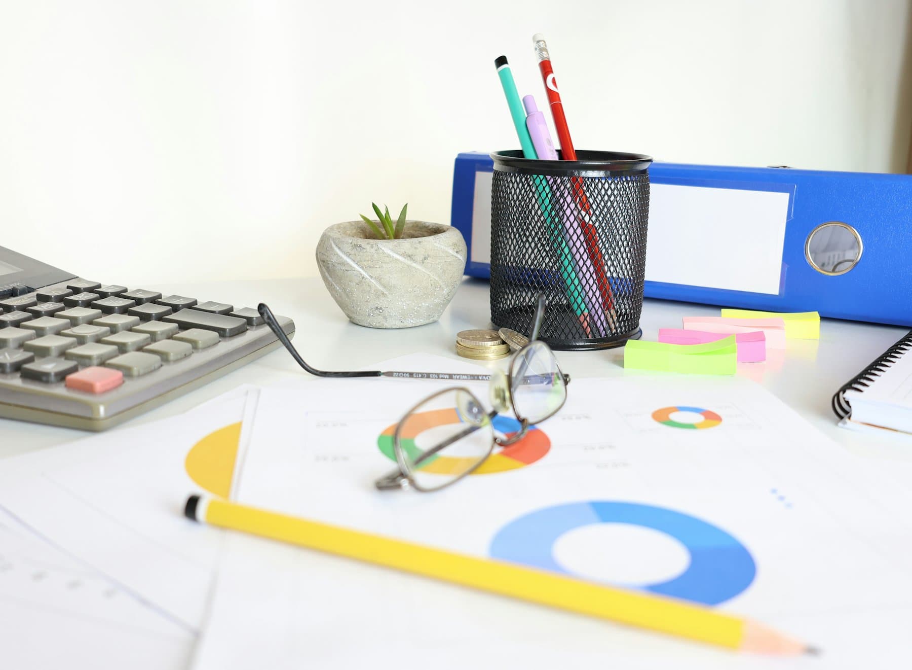 A desk with a calculator, printed charts, glasses and office supplies