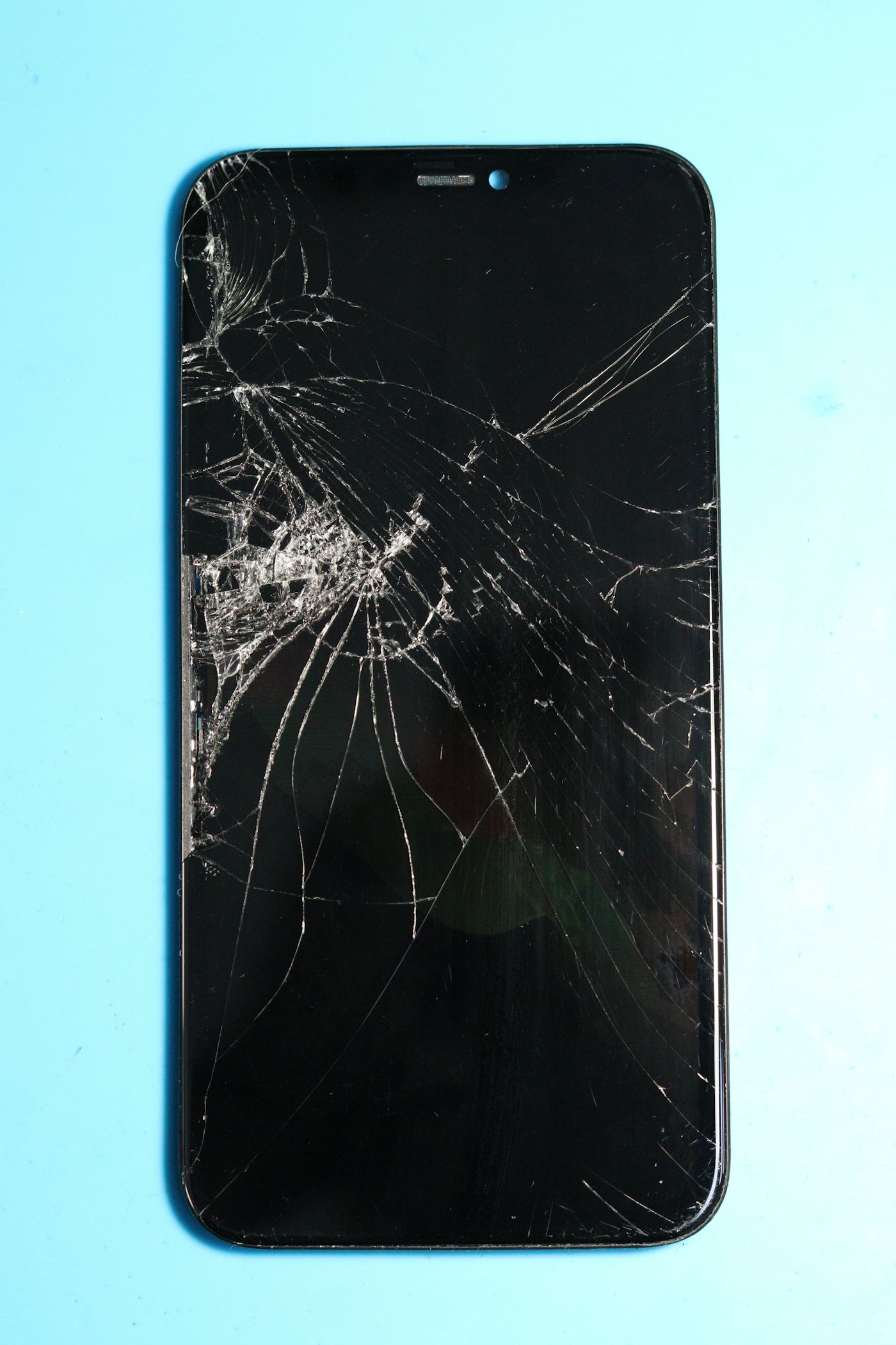 A smartphone with a shattered screen resting on a blue surface