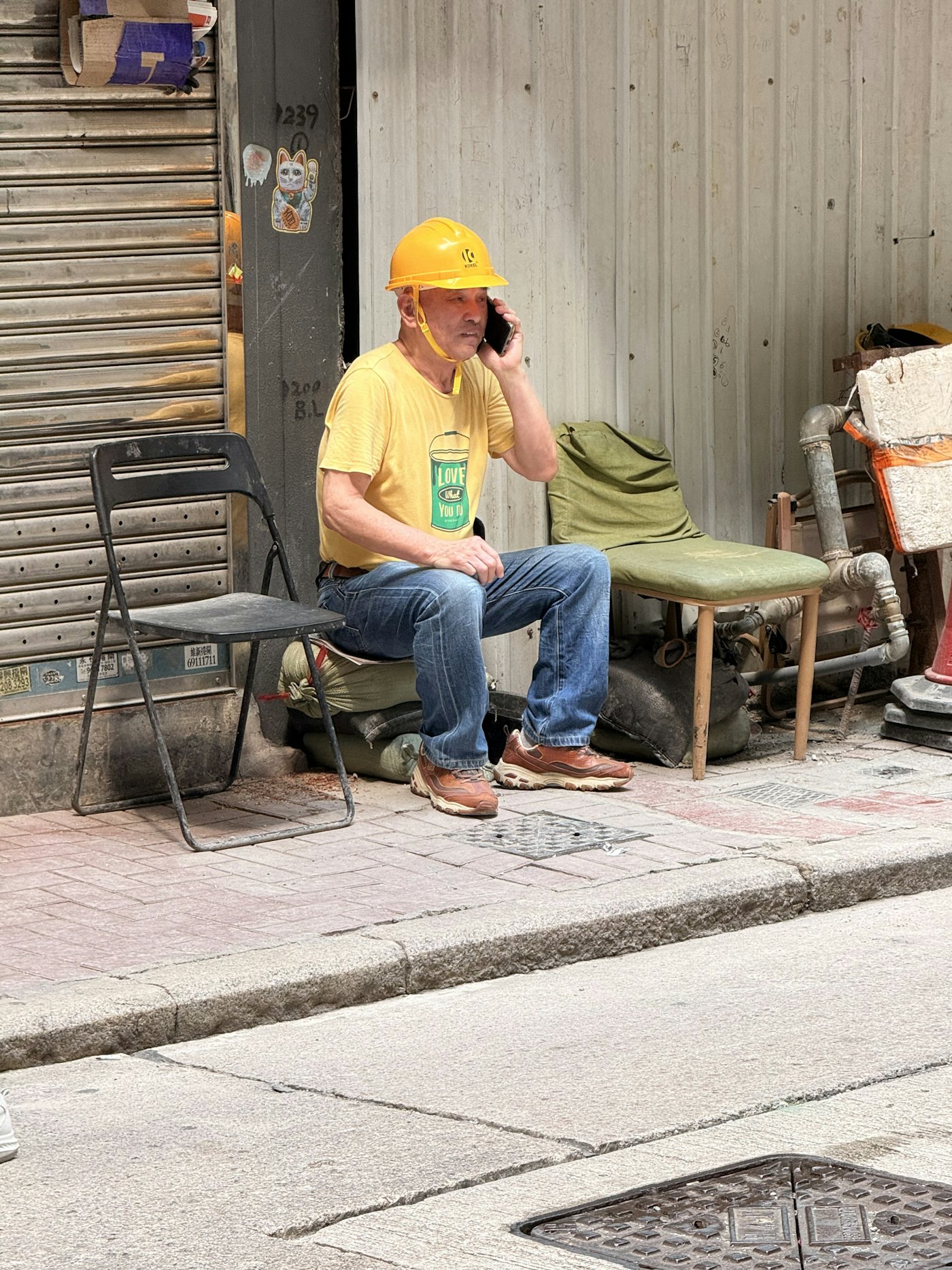 A worker in a hard hat taking a call on a pavement outside a site