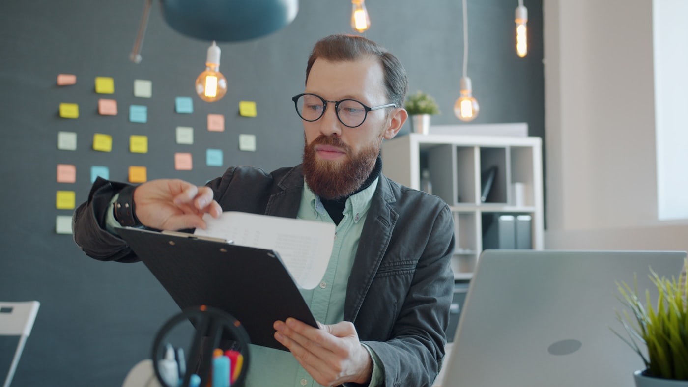 A person in glasses reviewing printed documents at a desk